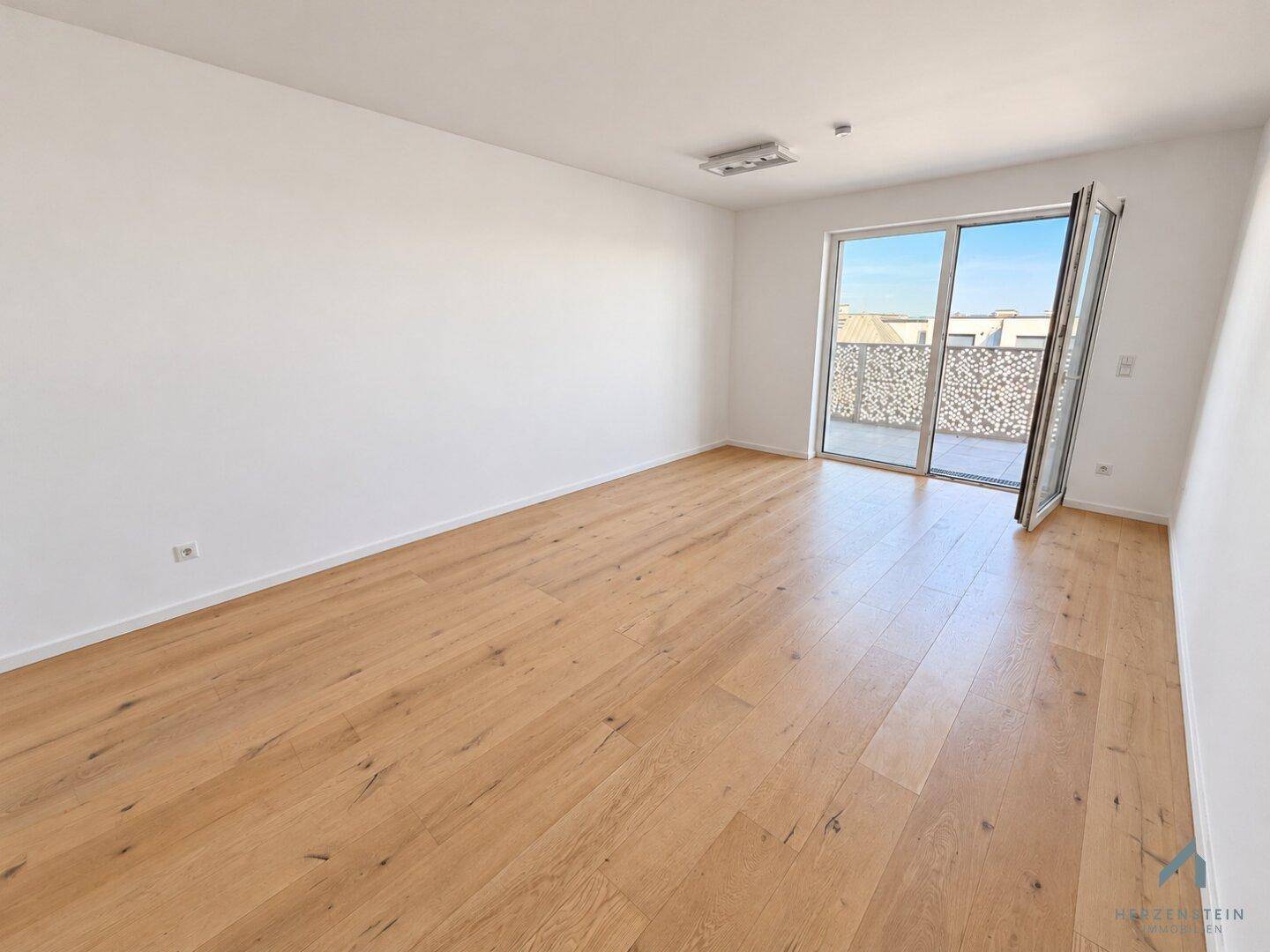 Geräumiger Wohnbereich mit Holzparkett und breiter Balkontür, die viel Licht spendet.
