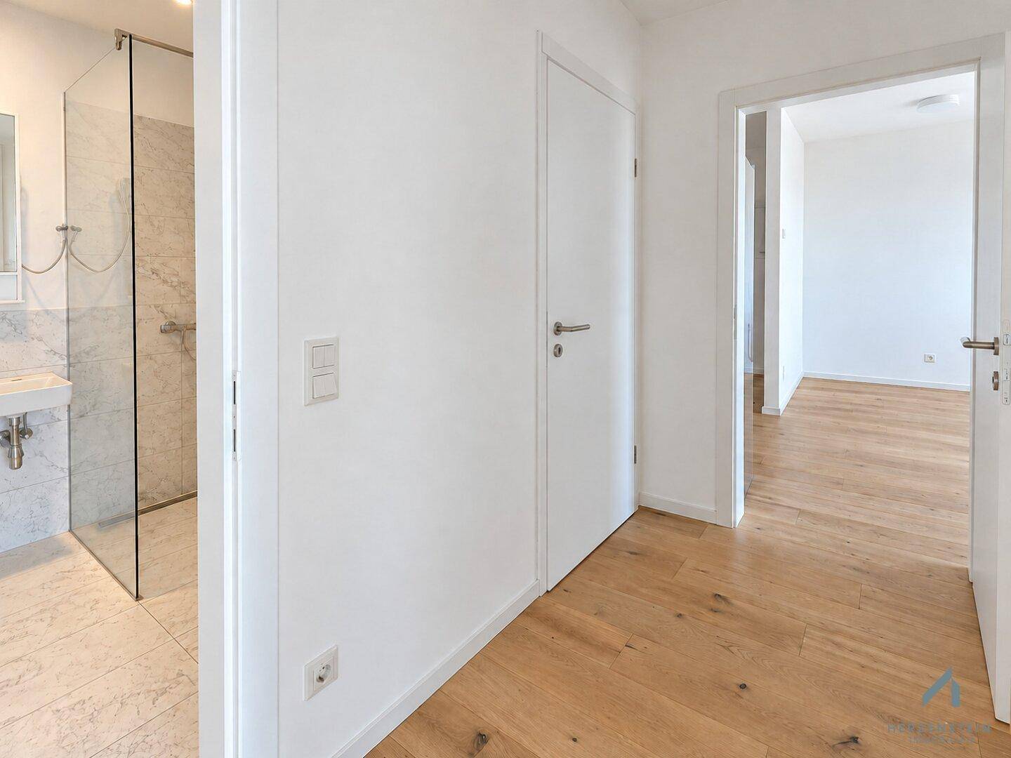 Heller Flur mit Holzparkett, der zu verschiedenen Zimmern und dem Badezimmer führt.