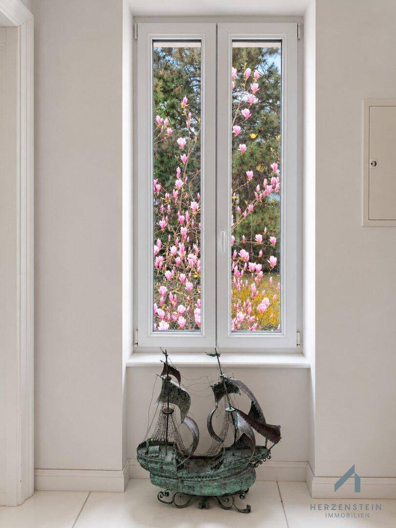 Heller Flur mit Fenster und Blick auf blühende Magnolienbäume, dekoriert mit einem Schiffsmodell.