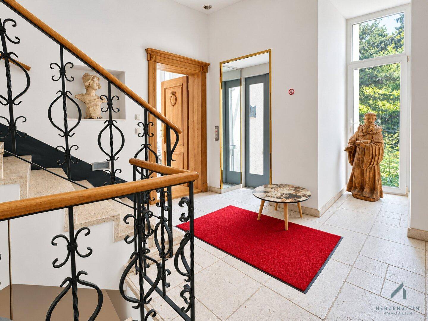 Eleganter Eingangsbereich mit Treppe, Aufzug und dekorativen Statuen.