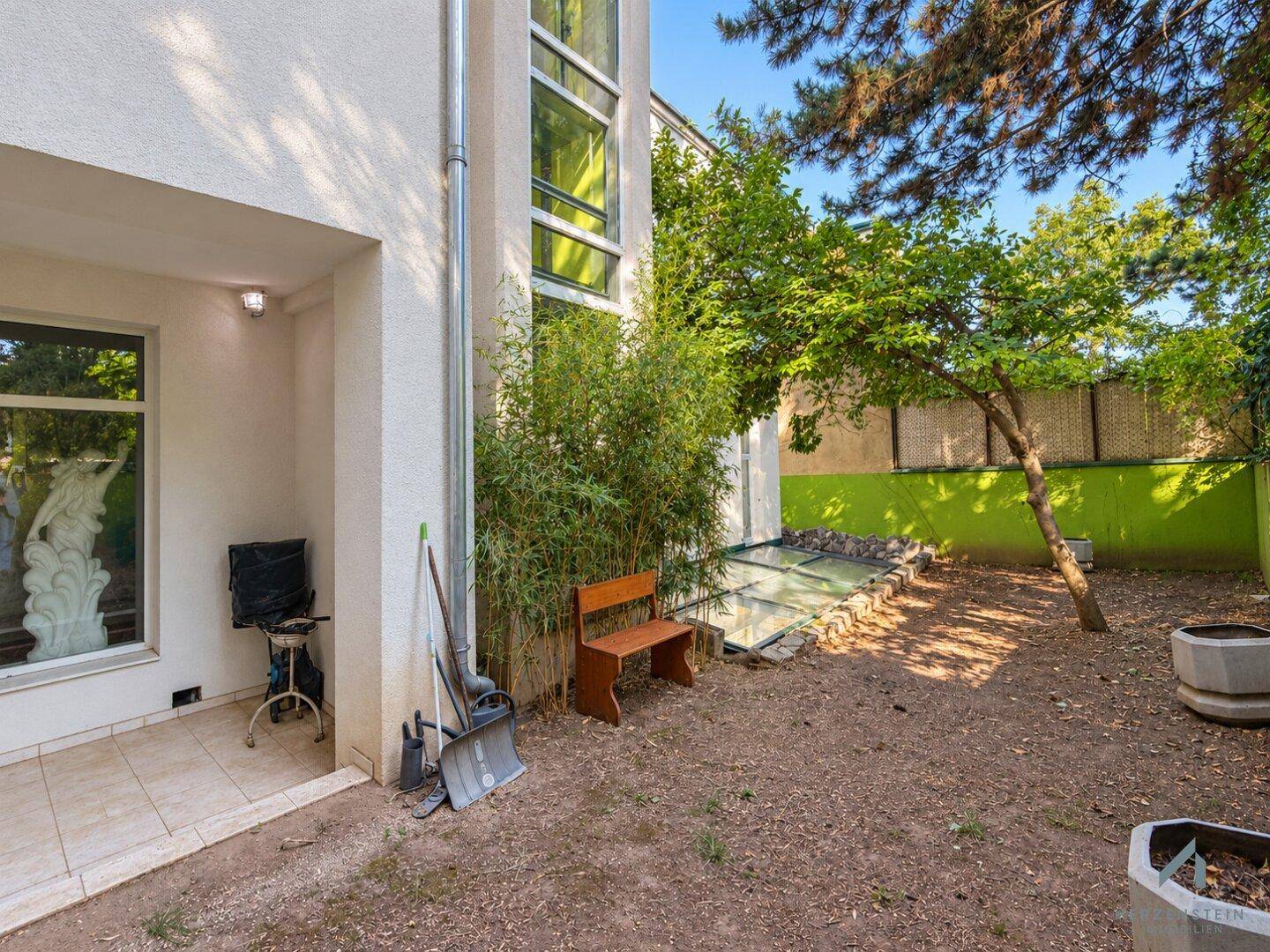 Kleiner Gartenbereich mit Sitzbank, Bambuspflanzen und Blick auf die Hausfassade.