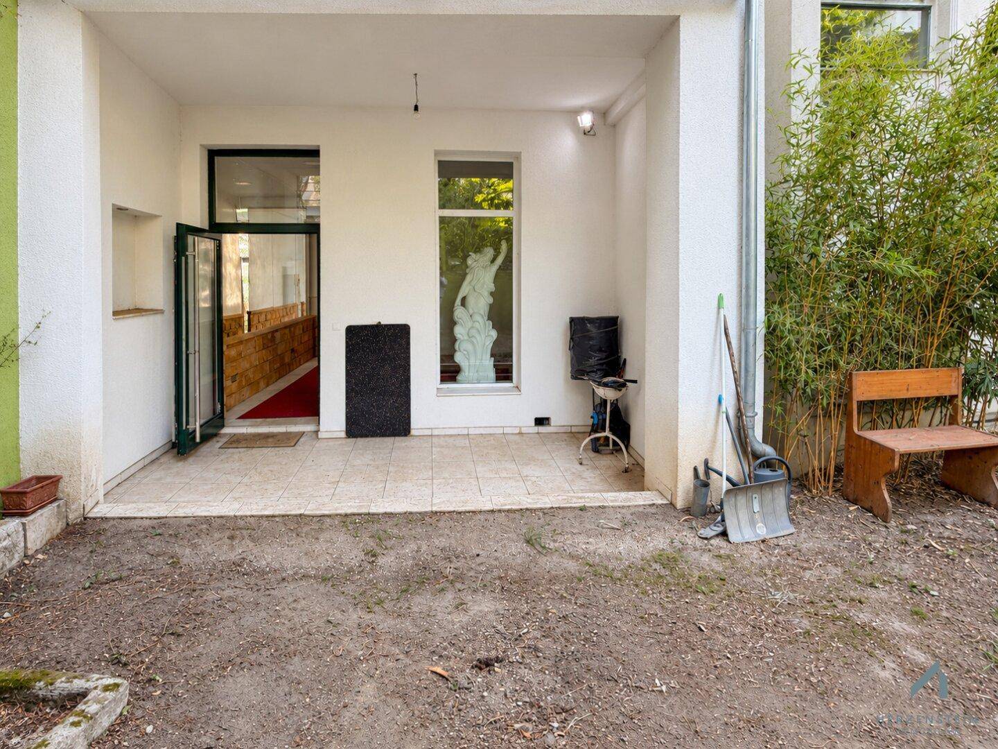 Überdachte Terrasse mit Fliesenboden, Grill und Blick in den Garten.