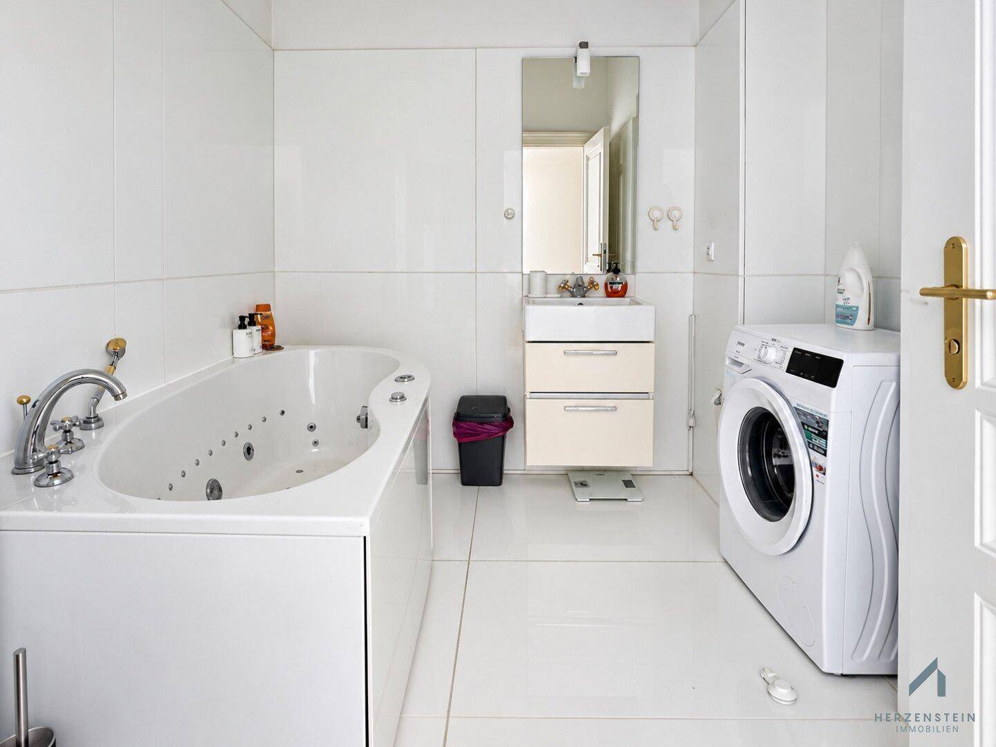 Modernes Badezimmer mit Whirlpool-Badewanne, Waschmaschine und weiß gefliesten Wänden.
