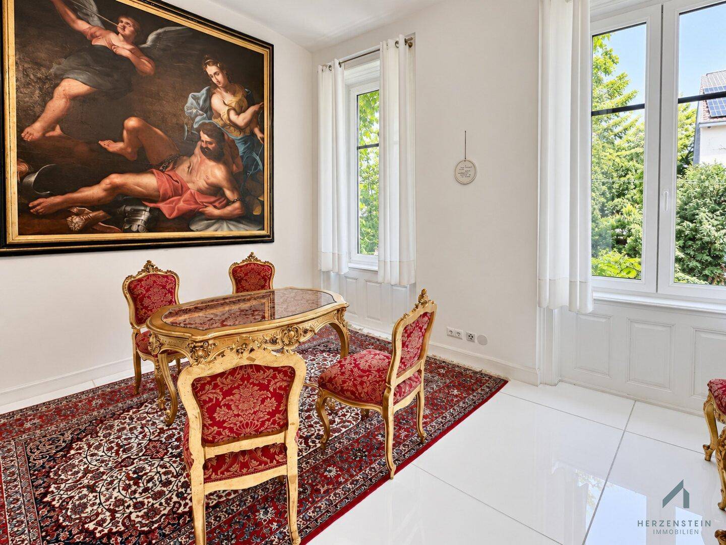Klassischer Essbereich mit vergoldetem Tisch, roten Stühlen und großem Gemälde an der Wand.