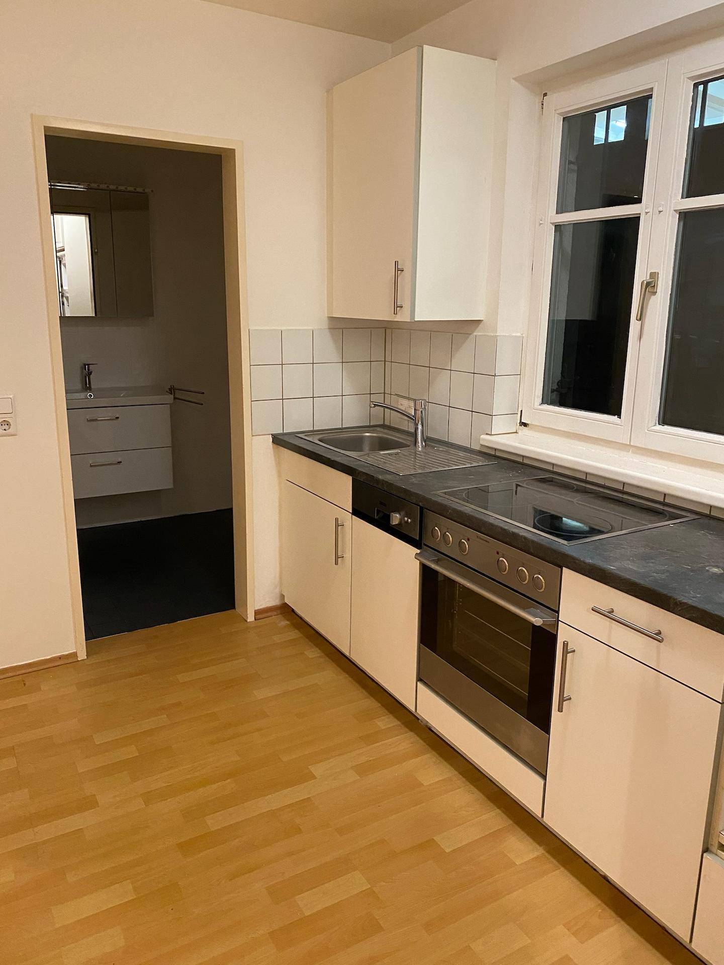 Funktionale Küche mit weißen Unterschränken, integriertem Backofen und Zugang zum Badezimmer.
