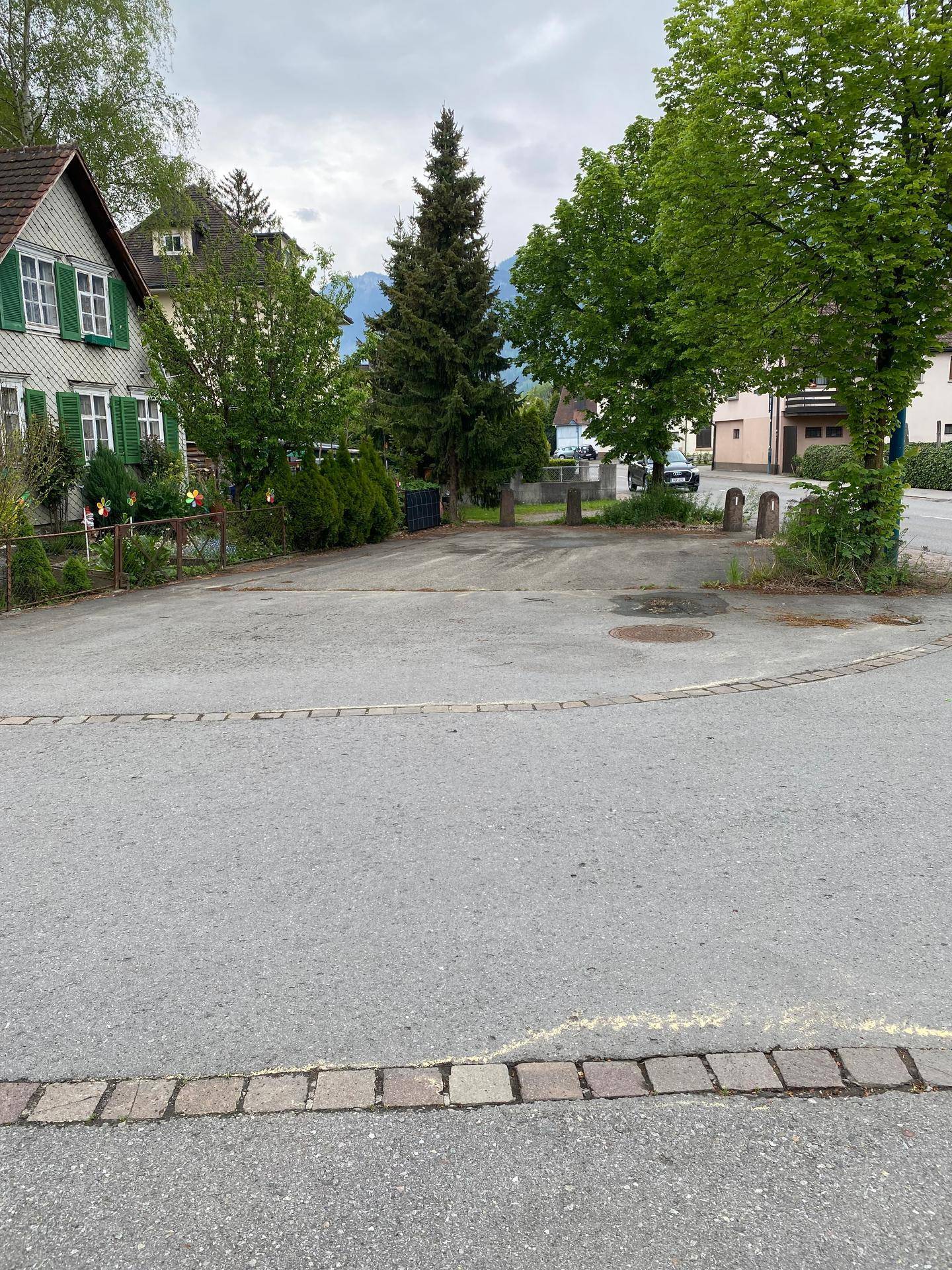 Außenbereich mit Parkplätzen, umgeben von Bäumen und Wohnhäusern in ländlicher Umgebung.