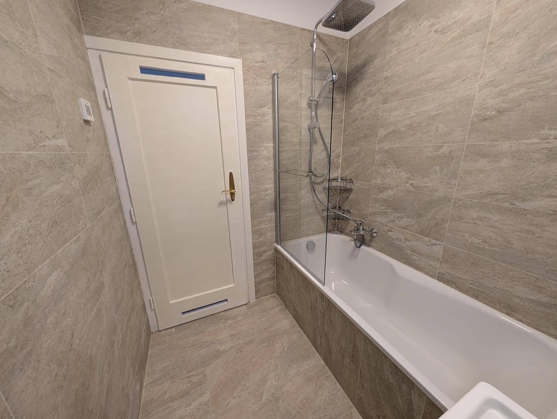 Helles Badezimmer mit Badewanne, Duschabtrennung und modernen Fliesen, bietet Komfort und Funktionalität.