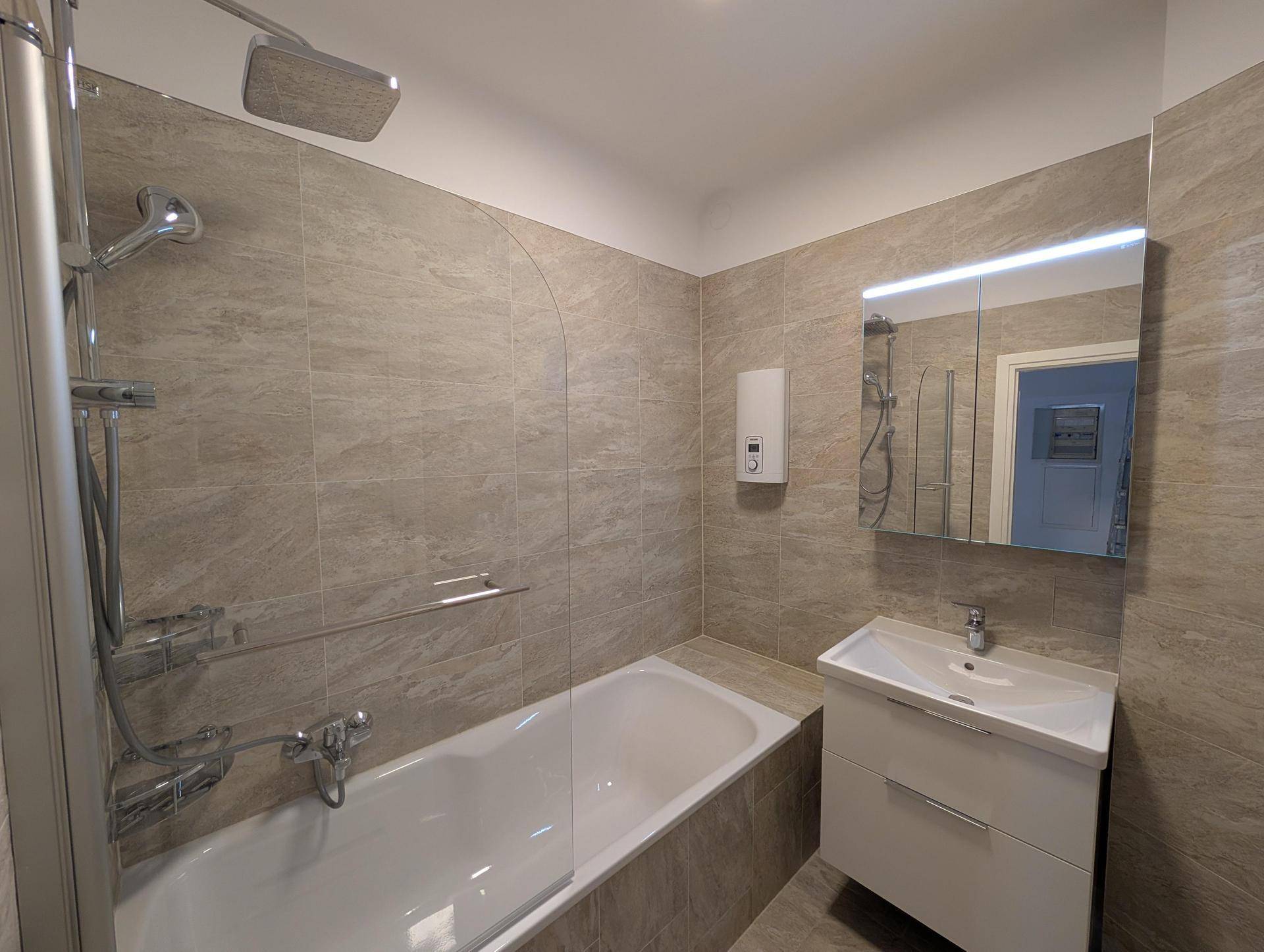 Modernes Badezimmer mit hellgrauen Fliesen, Badewanne mit Duschfunktion und Waschtisch mit Spiegelschrank.