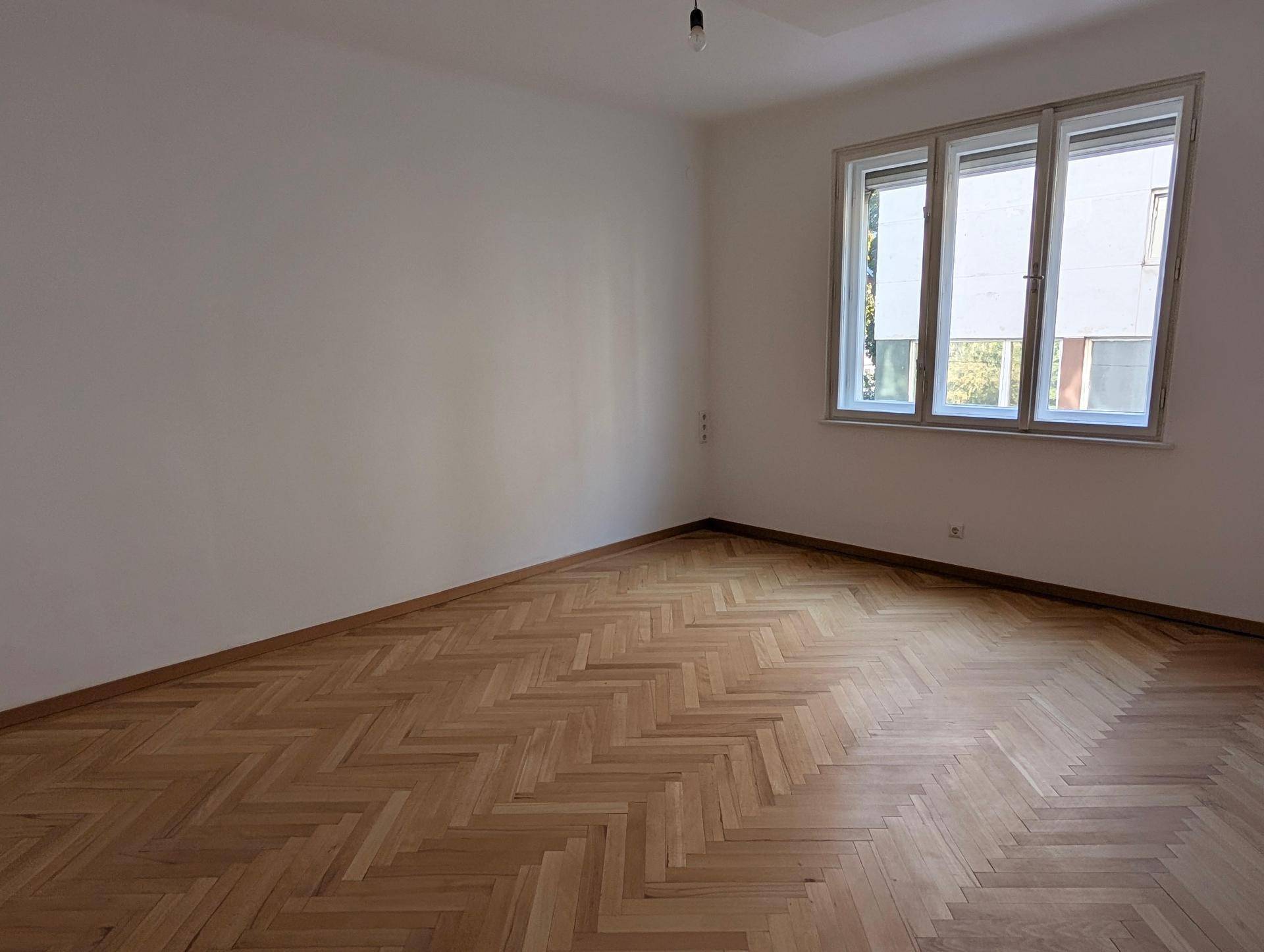 Geräumiges Zimmer mit klassischem Fischgrätparkett und großen Fenstern für viel Tageslicht.