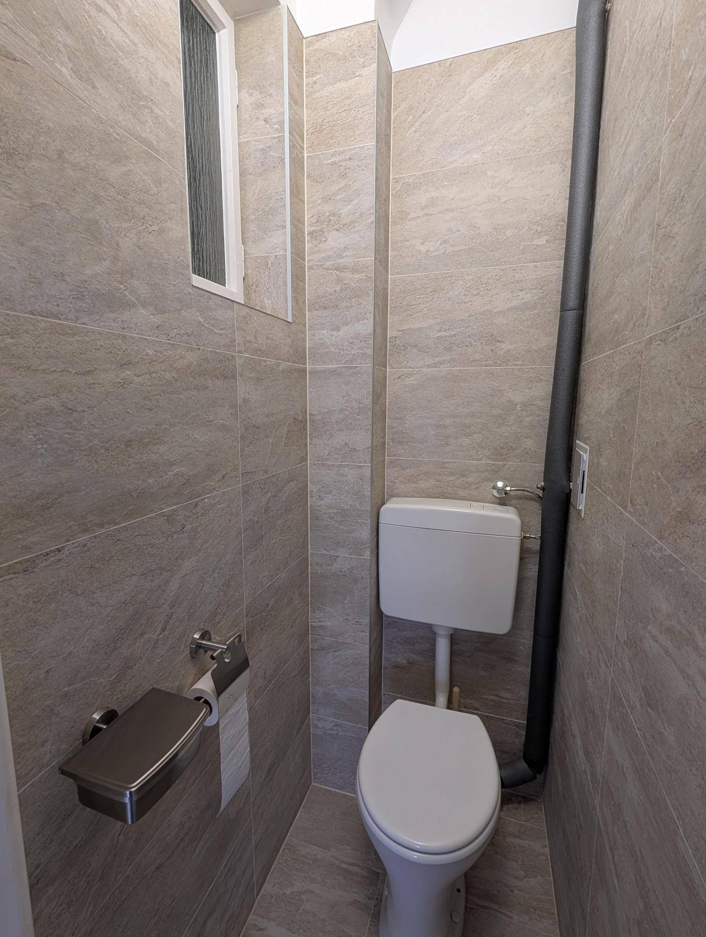 Separates WC mit modernen Fliesen, Toilette und kleinem Fenster für natürliche Belüftung.