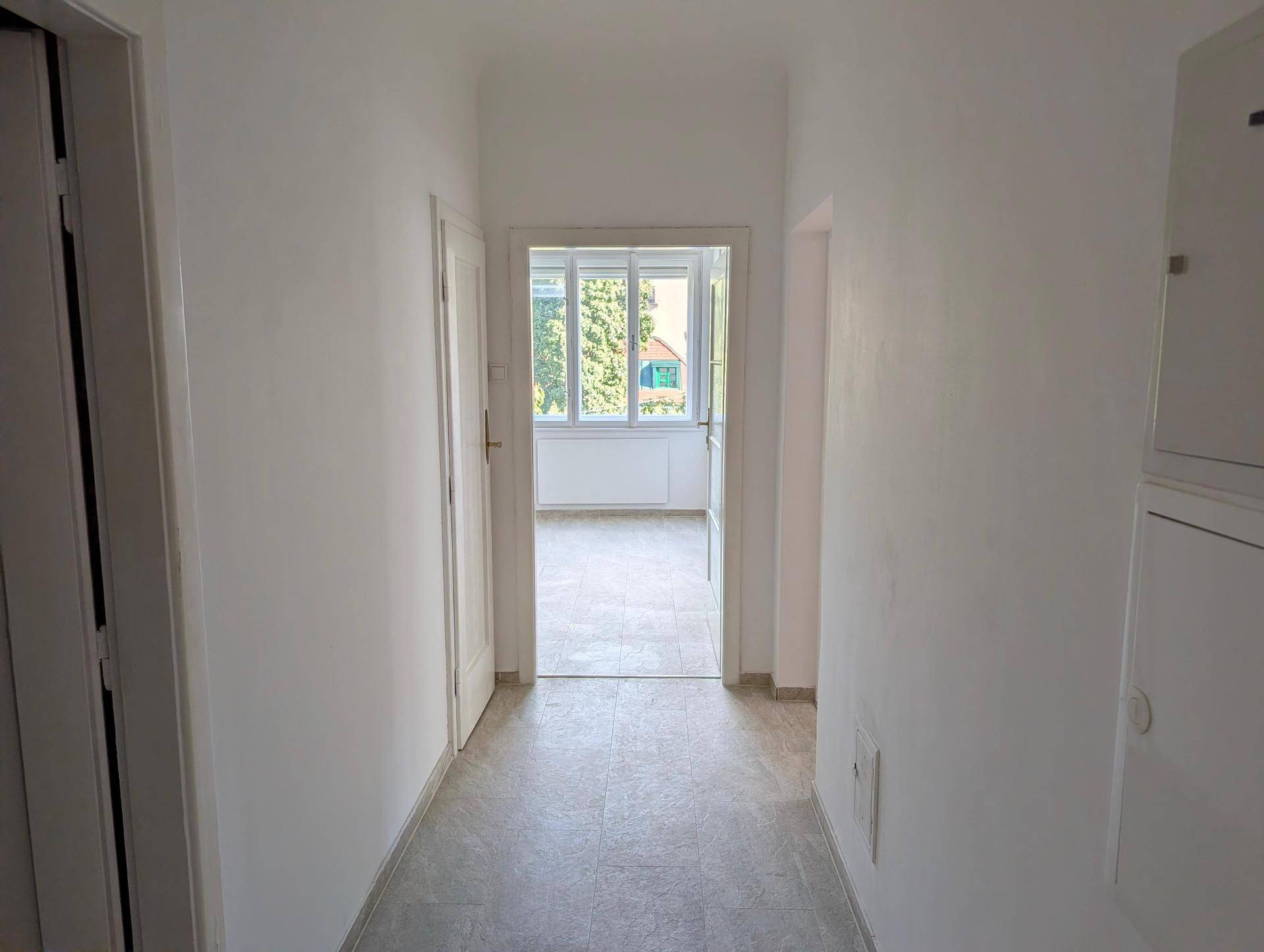 Heller Flur mit modernen Fliesen und Durchgang zu einem weiteren Zimmer mit Fenster.