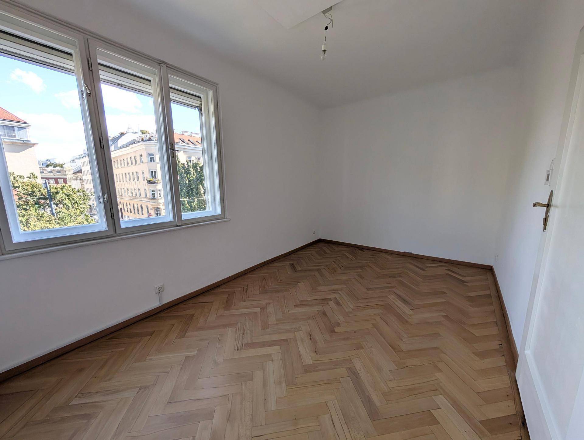 Helles Zimmer mit Fischgrätparkett und weitem Blick über die Stadt und grüne Bäume.