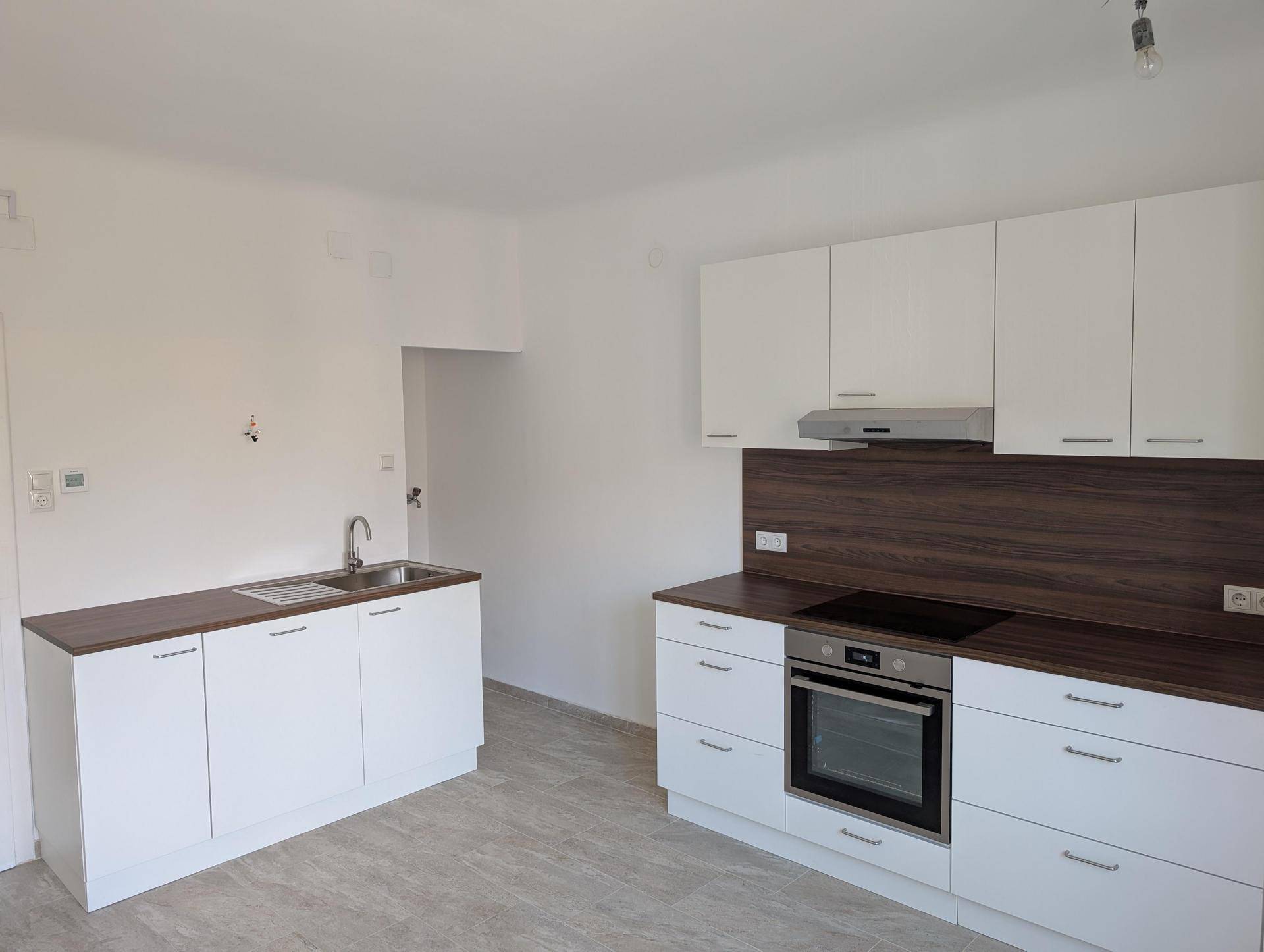 Moderne Einbauküche mit weißen Fronten, dunkler Arbeitsplatte und integrierten Geräten.