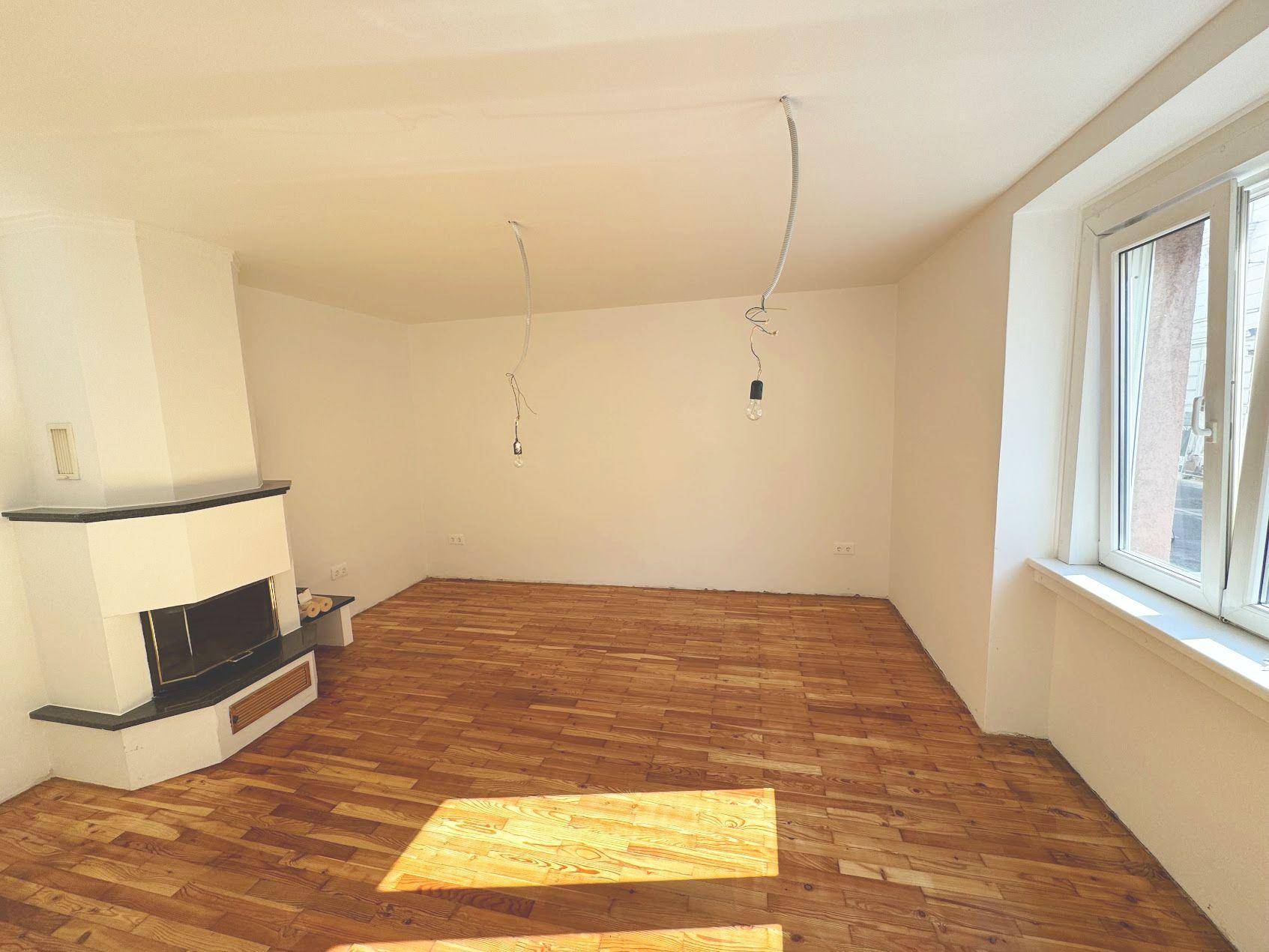 Helles Wohnzimmer mit Parkettboden, Kamin und großen Fenstern, bereit zur individuellen Gestaltung.