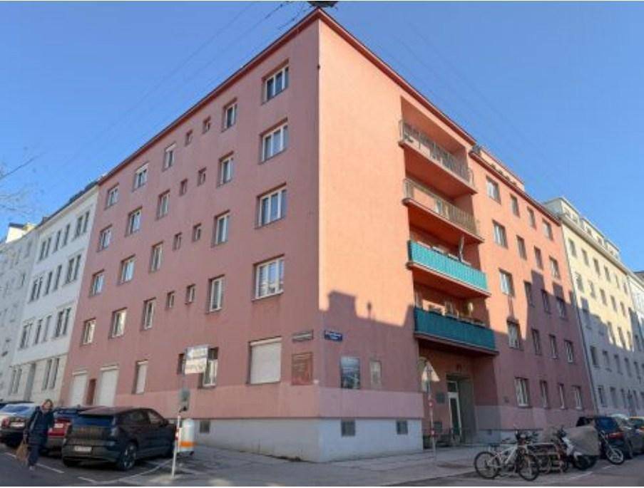 Mehrstöckiges Wohngebäude mit rosafarbener Fassade und Balkonen an einer städtischen Straße.