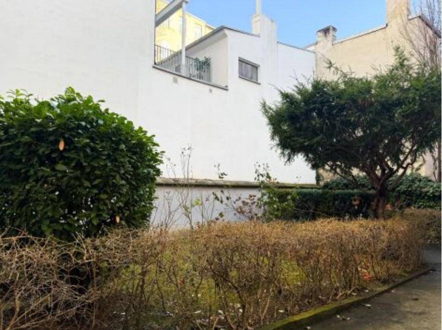 Gartenbereich mit Sträuchern und Blick auf die Rückseite eines Gebäudes mit Balkon.