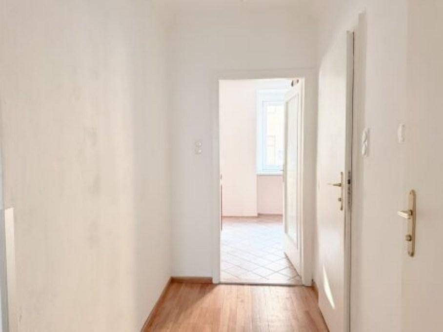 Langer, heller Flur mit Holzboden, der zu einem weiteren Raum mit Fliesenboden führt.