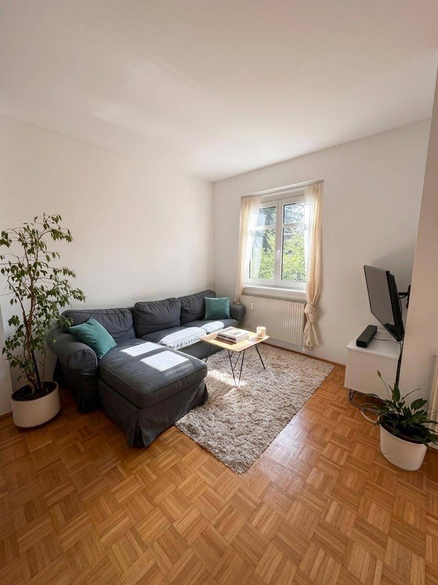 Gemütliches Wohnzimmer mit großem Sofa, Teppich und Parkettboden, hell durch ein Fenster.