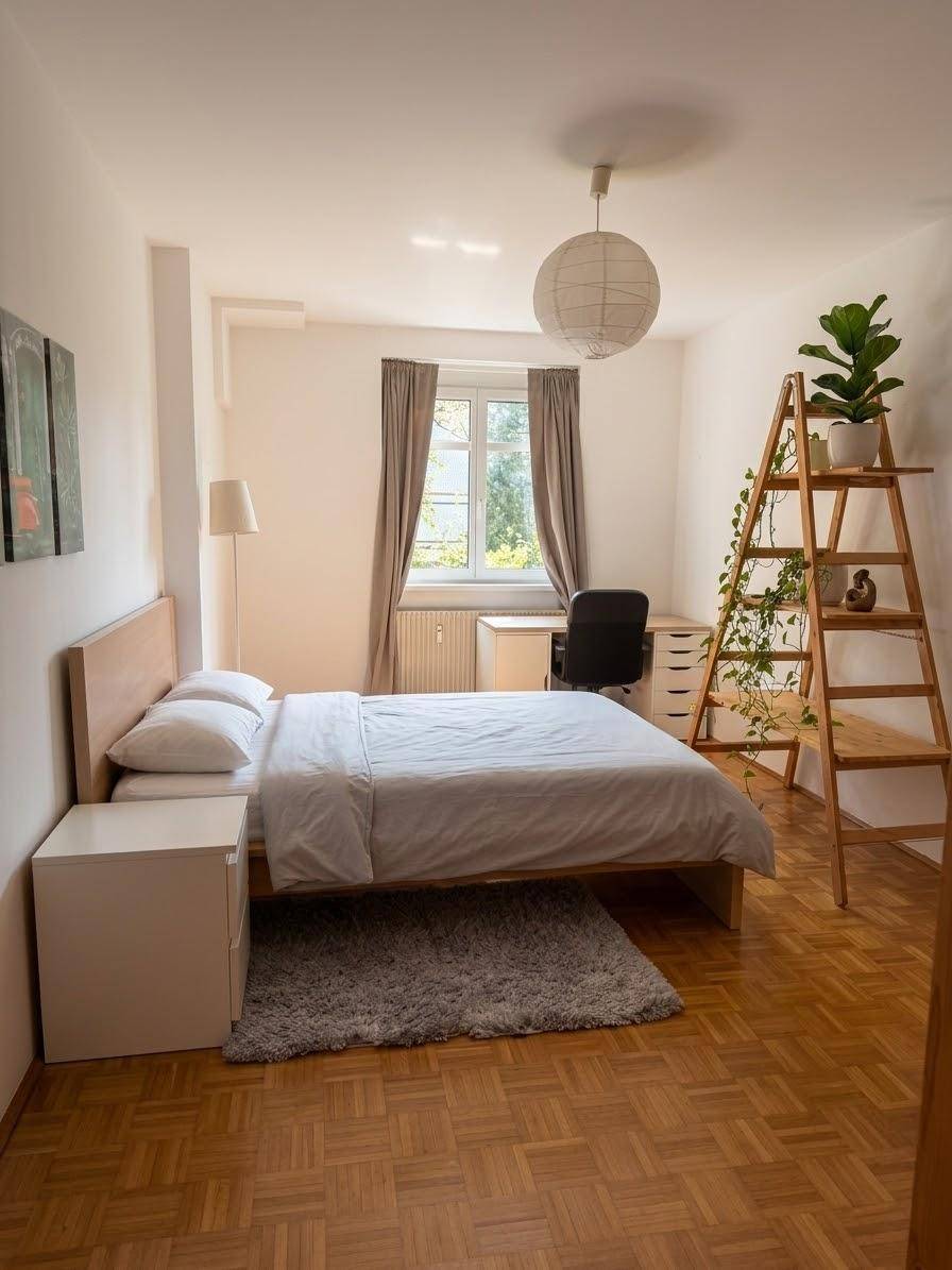 Helles Schlafzimmer mit Holzbett, Schreibtisch und Parkettboden, gut beleuchtet durch ein Fenster.
