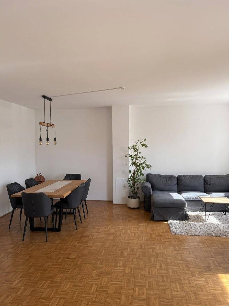 Offener Wohn- und Essbereich mit Holztisch, bequemer Couch und durchgehendem Parkettboden.