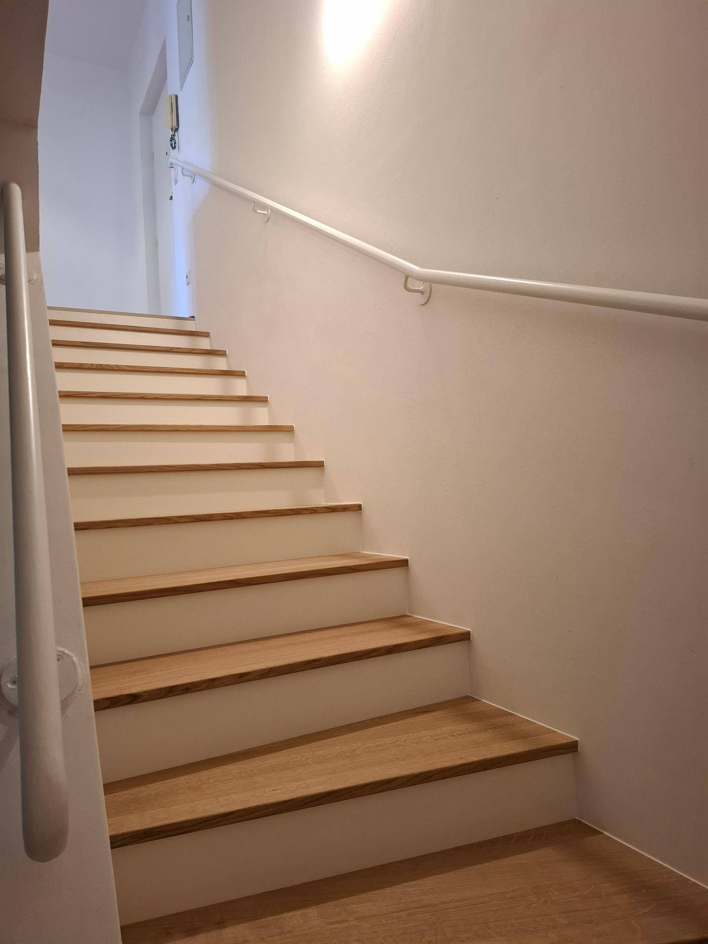 Helle Holztreppe mit weißem Geländer, die die verschiedenen Etagen des Hauses verbindet.