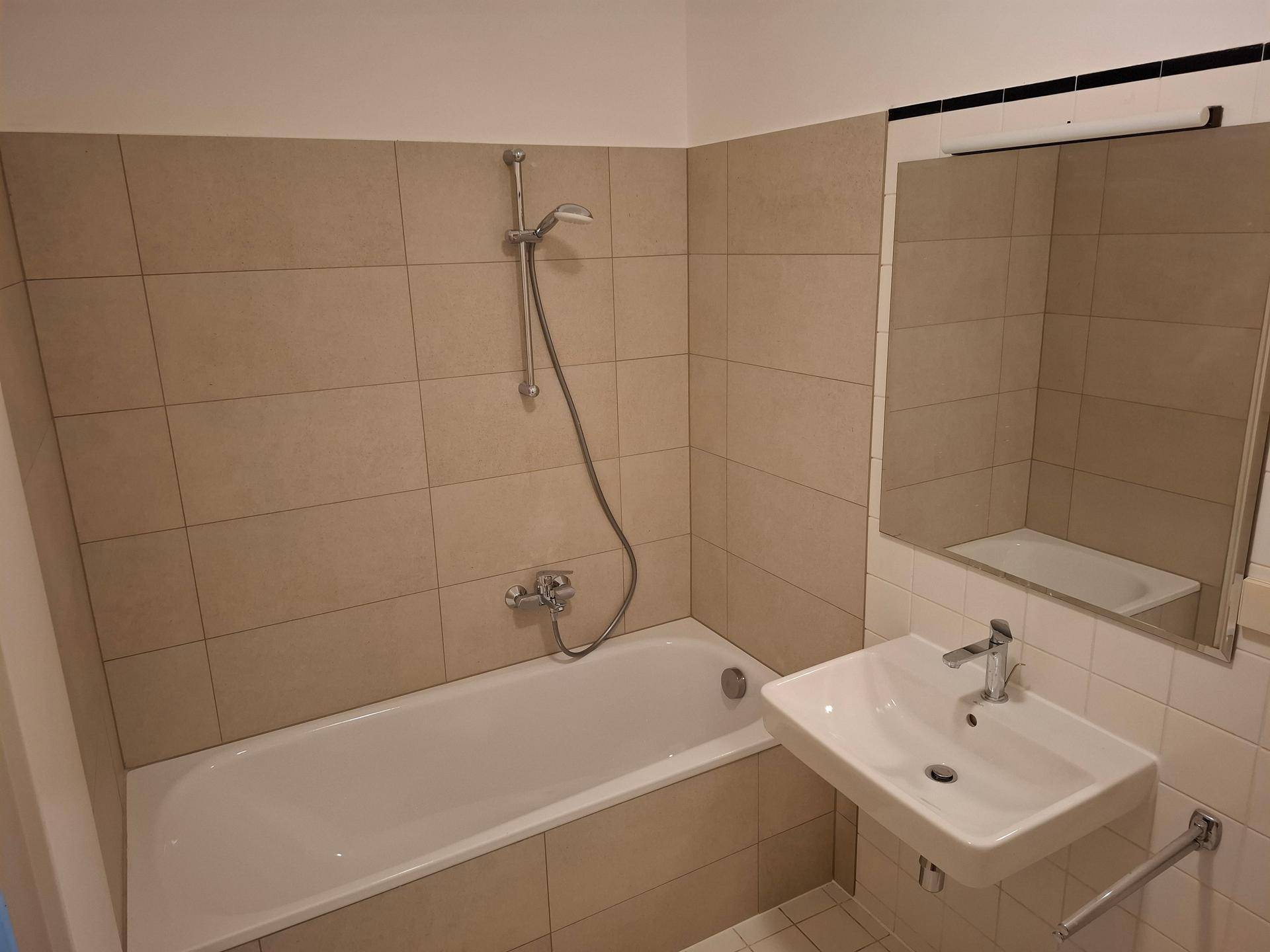 Badezimmer mit beigefarbenen Fliesen, Badewanne mit Duschfunktion und modernem Waschbecken.