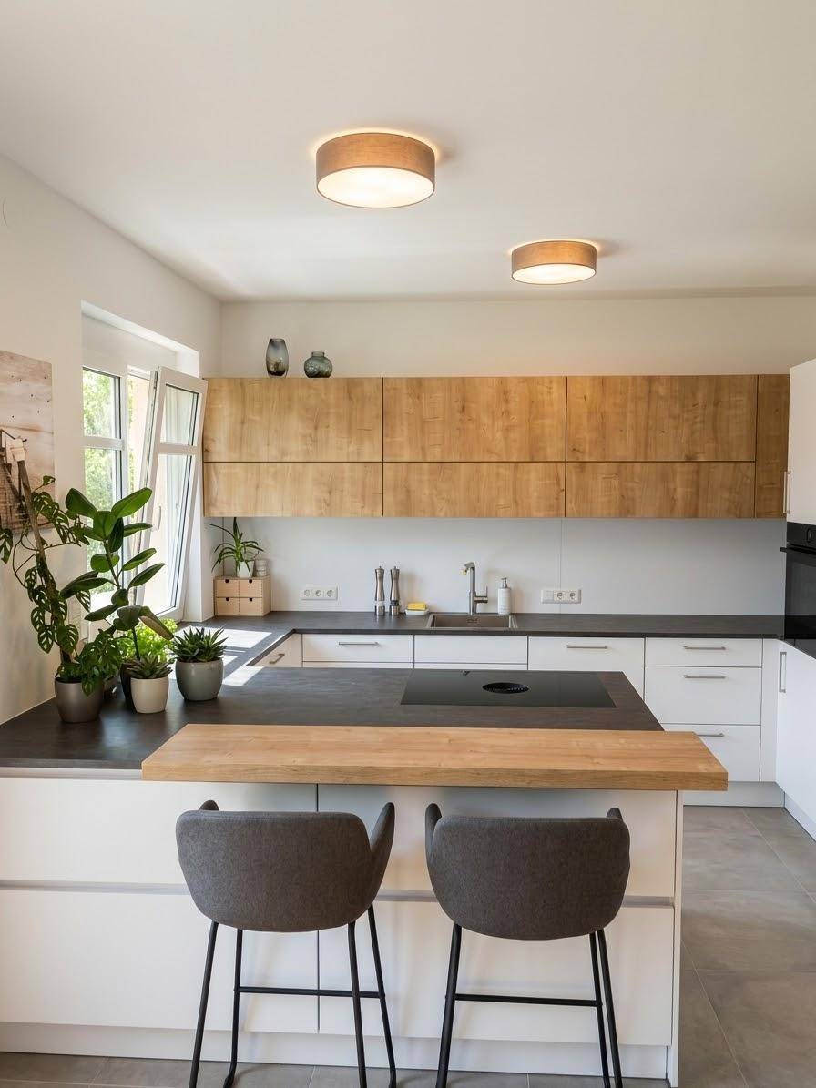 Moderne Küche mit Holzschränken, dunkler Arbeitsplatte, Induktionskochfeld und viel Tageslicht.