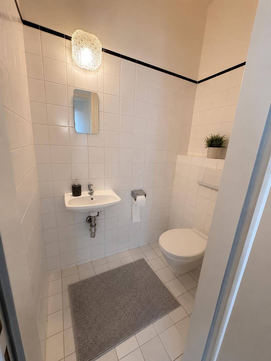 Kleines Gäste-WC mit weißen Fliesen, wandhängendem WC und einem kompakten Waschbecken.