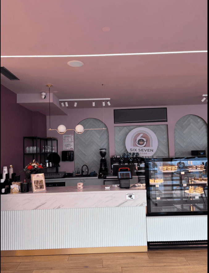 Die Theke des Cafés mit Kaffeemaschine, Kuchenvitrine und modernem Design in Rosa- und Weißtönen.