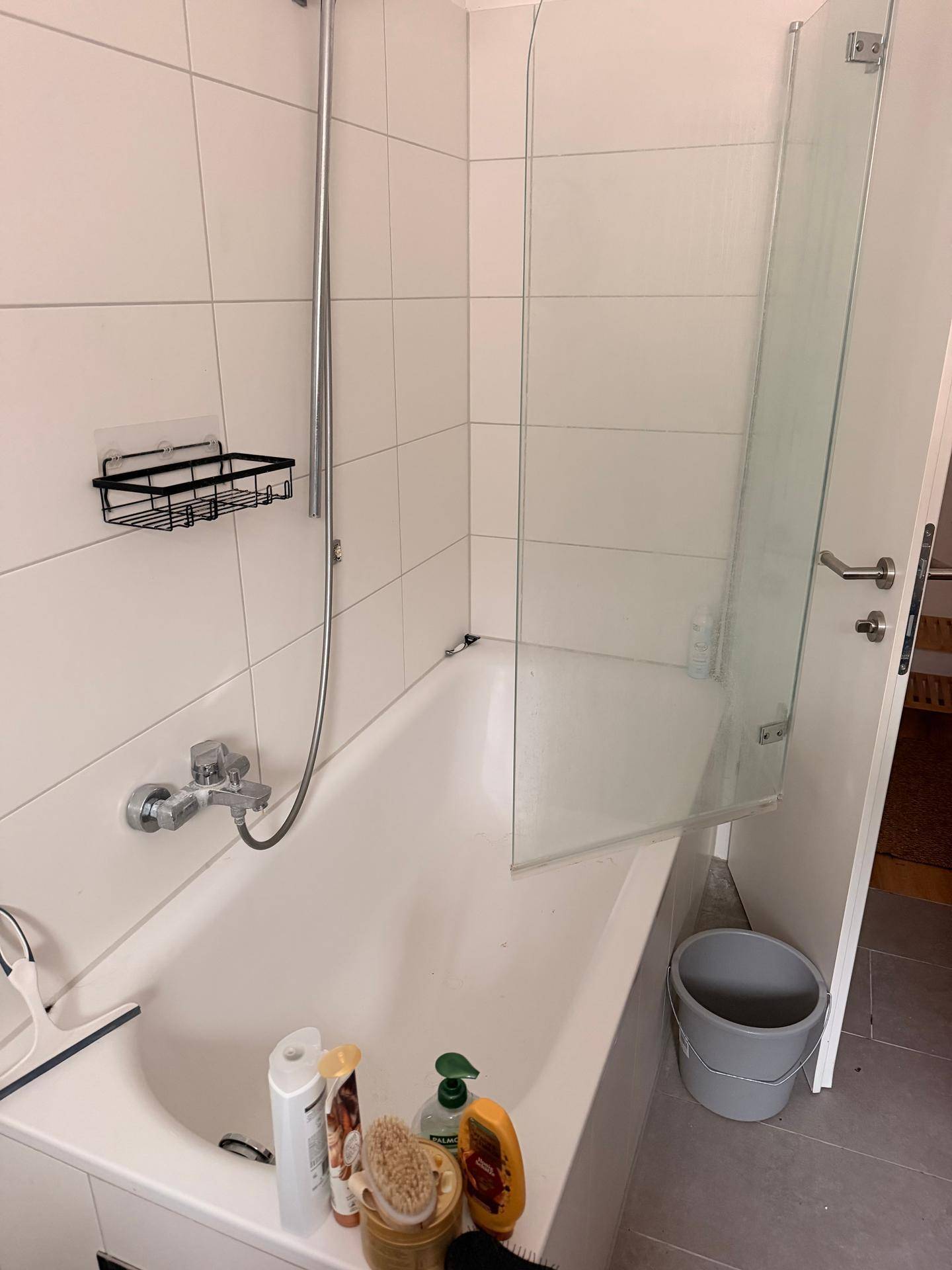 Badewanne mit Duschabtrennung und Fliesenwänden in einem hellen Badezimmer.