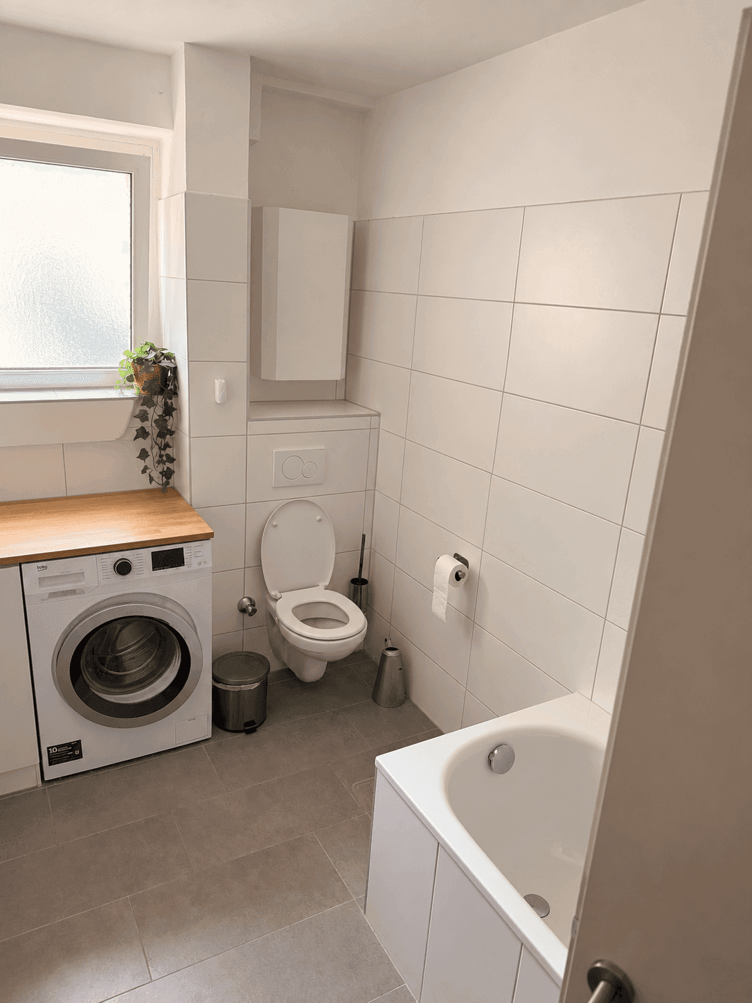 Modernes Badezimmer mit Badewanne, Toilette, Waschmaschine und Fenster.