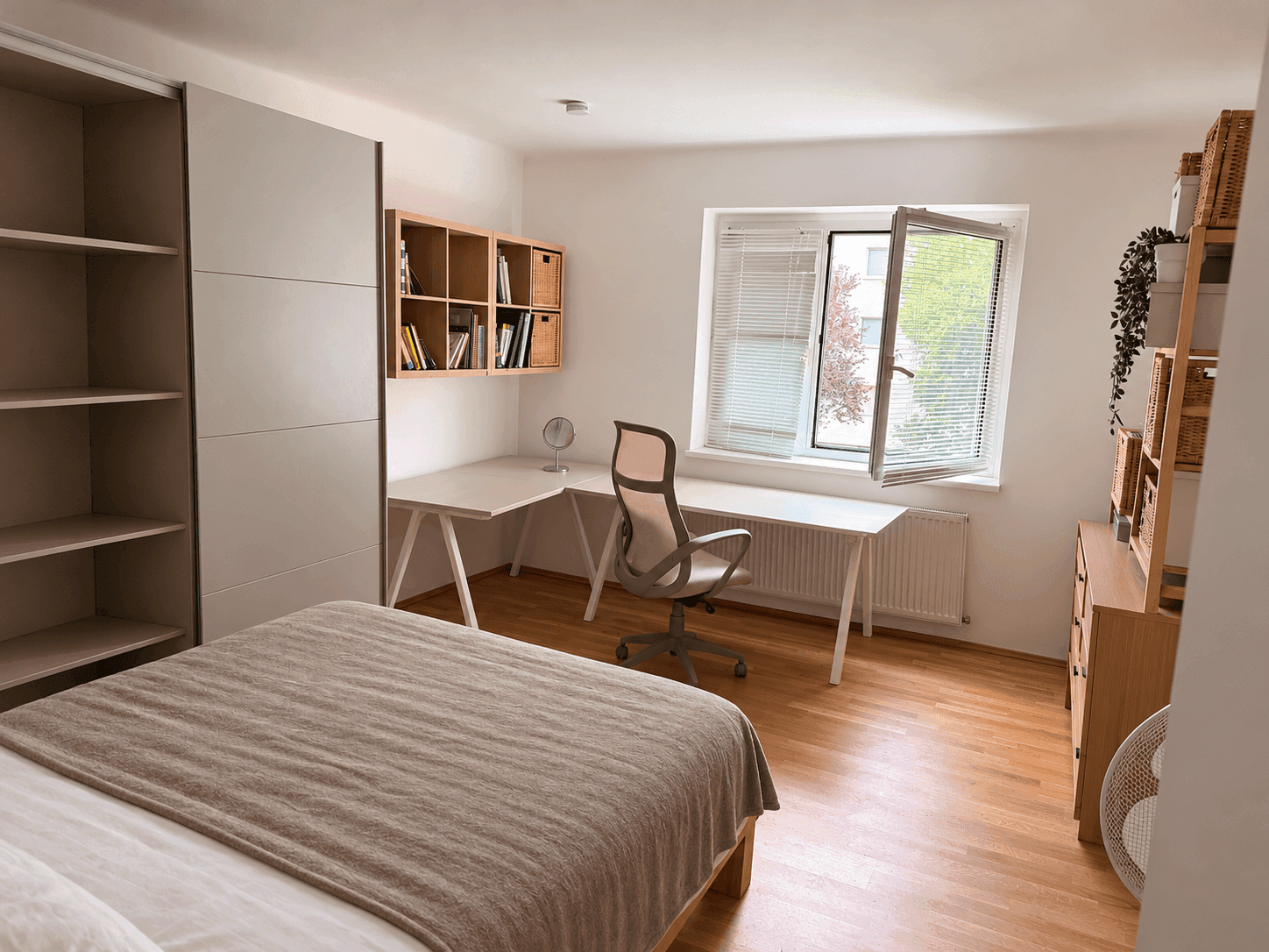 Schlafzimmer mit Holzboden, großem Fenster, Schreibtisch und Einbauschrank.