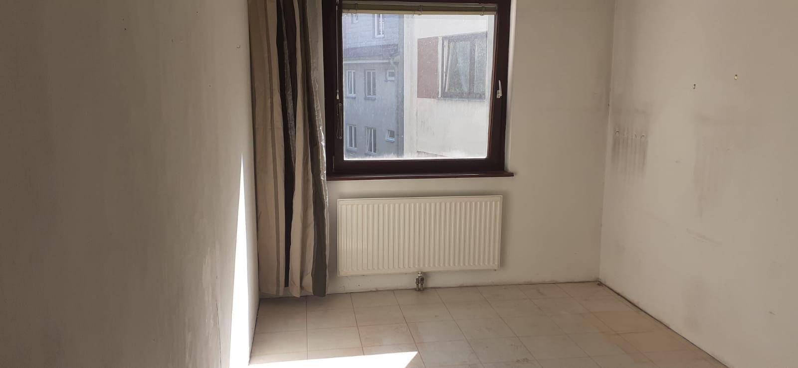 Leeres Zimmer mit Fenster, Heizkörper und Fliesenboden, bereit zur individuellen Gestaltung.