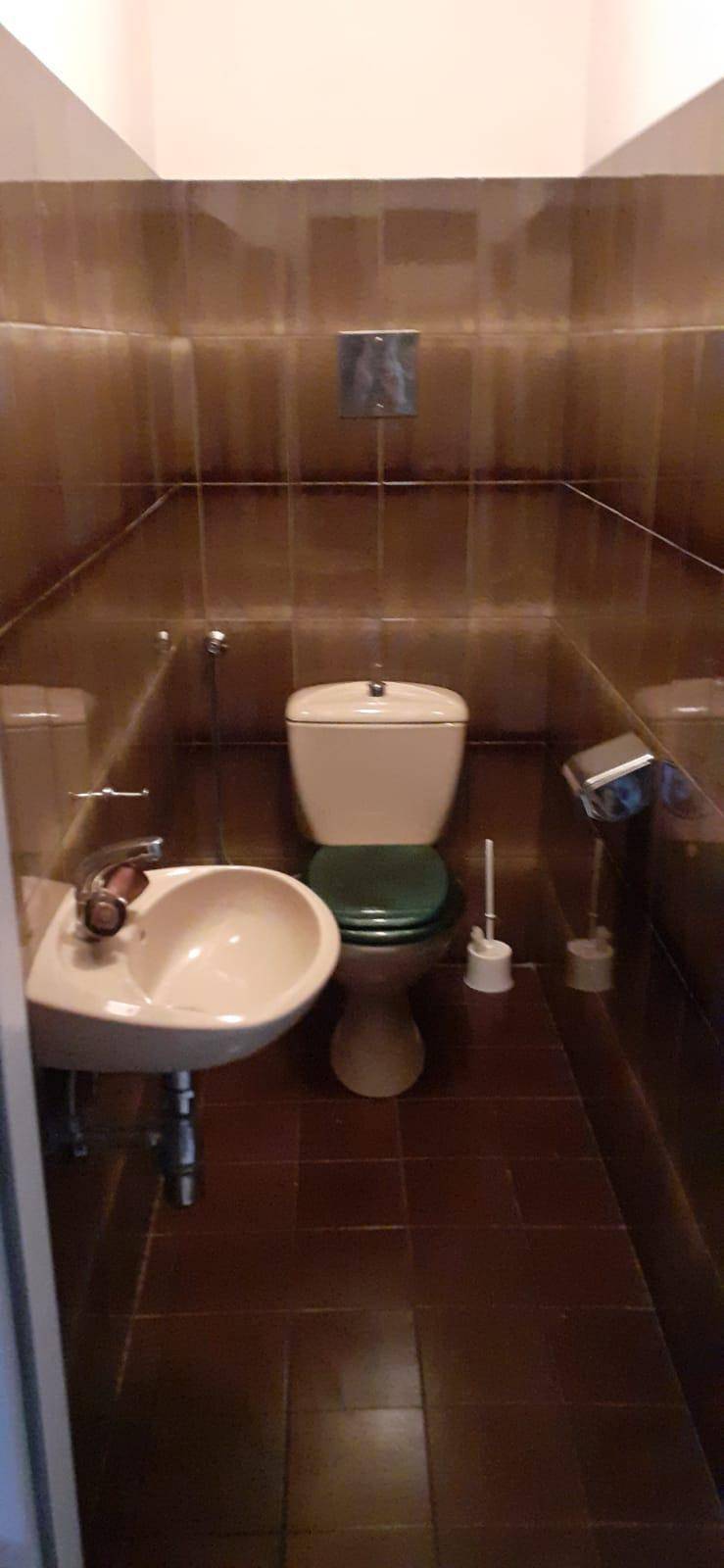 Kleines Gäste-WC mit braunen Fliesen, Toilette und Handwaschbecken.