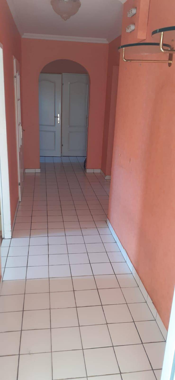 Geräumiger Flur mit Fliesenboden und orangefarbenen Wänden, führt zu einem Bogen und Doppeltüren.