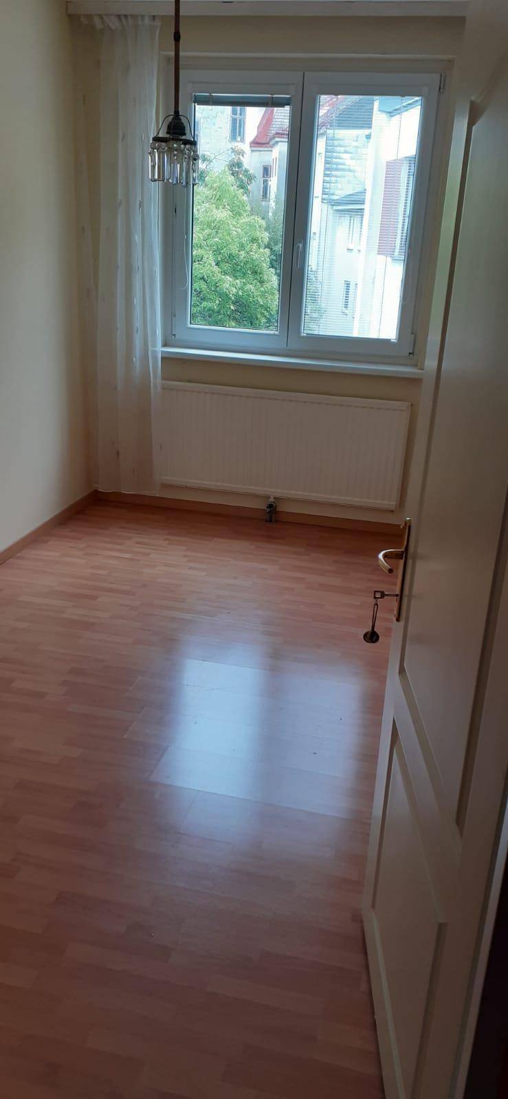 Helles Zimmer mit Holzboden, großem Fenster und Heizkörper, bereit zur Einrichtung.