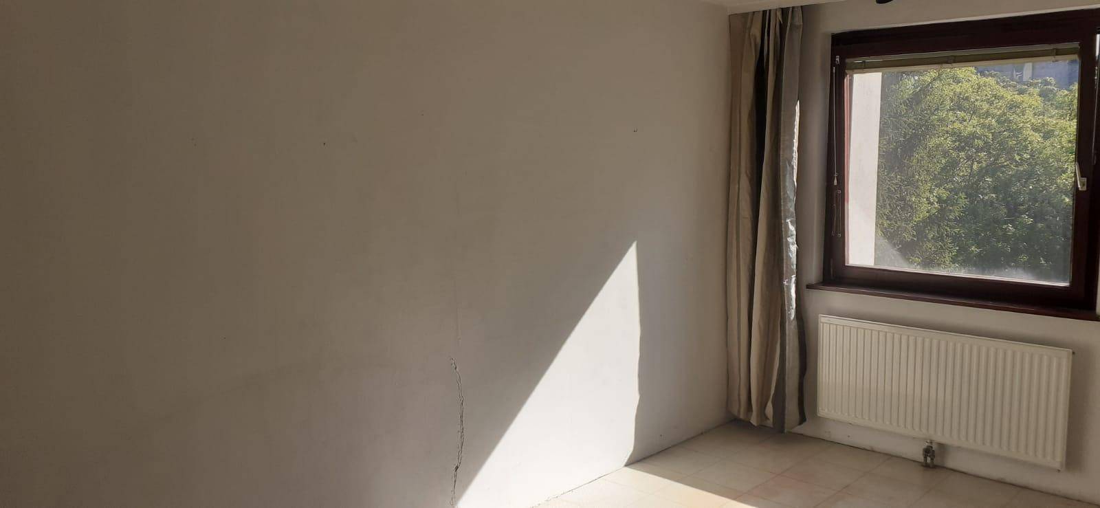 Helles Zimmer mit Fenster, Heizkörper und Vorhängen, ideal als Schlaf- oder Arbeitszimmer.