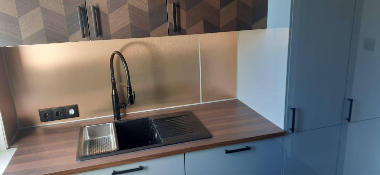 Moderne Küchenzeile mit schwarzer Spüle, Holz-Arbeitsplatte und gemusterten Oberschränken.