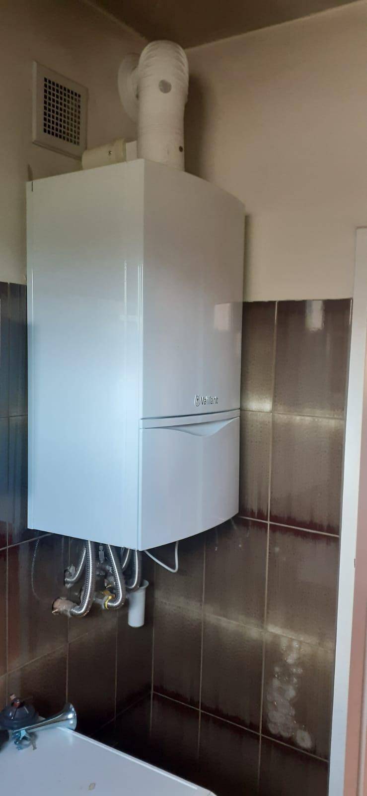 Weißer Heizkessel an einer gefliesten Wand, wahrscheinlich in einem Badezimmer installiert.