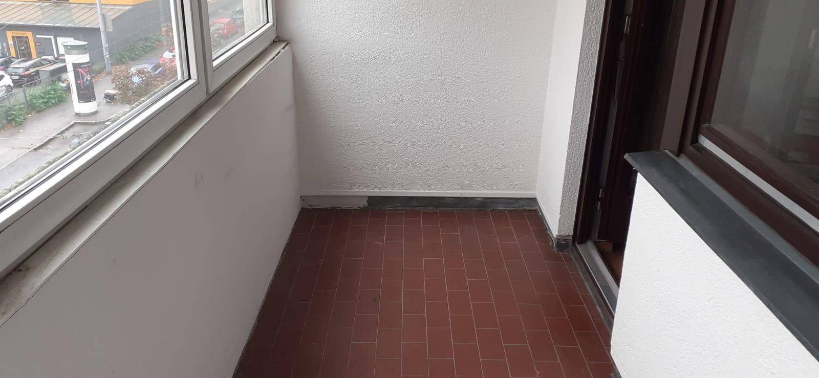 Heller, verglaster Balkon mit braunem Fliesenboden und Ausblick auf die städtische Umgebung.