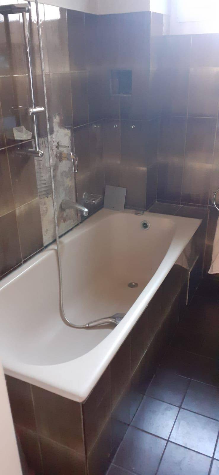 Badewanne mit Duschvorrichtung und Glasabtrennung in einem gefliesten Badezimmer.