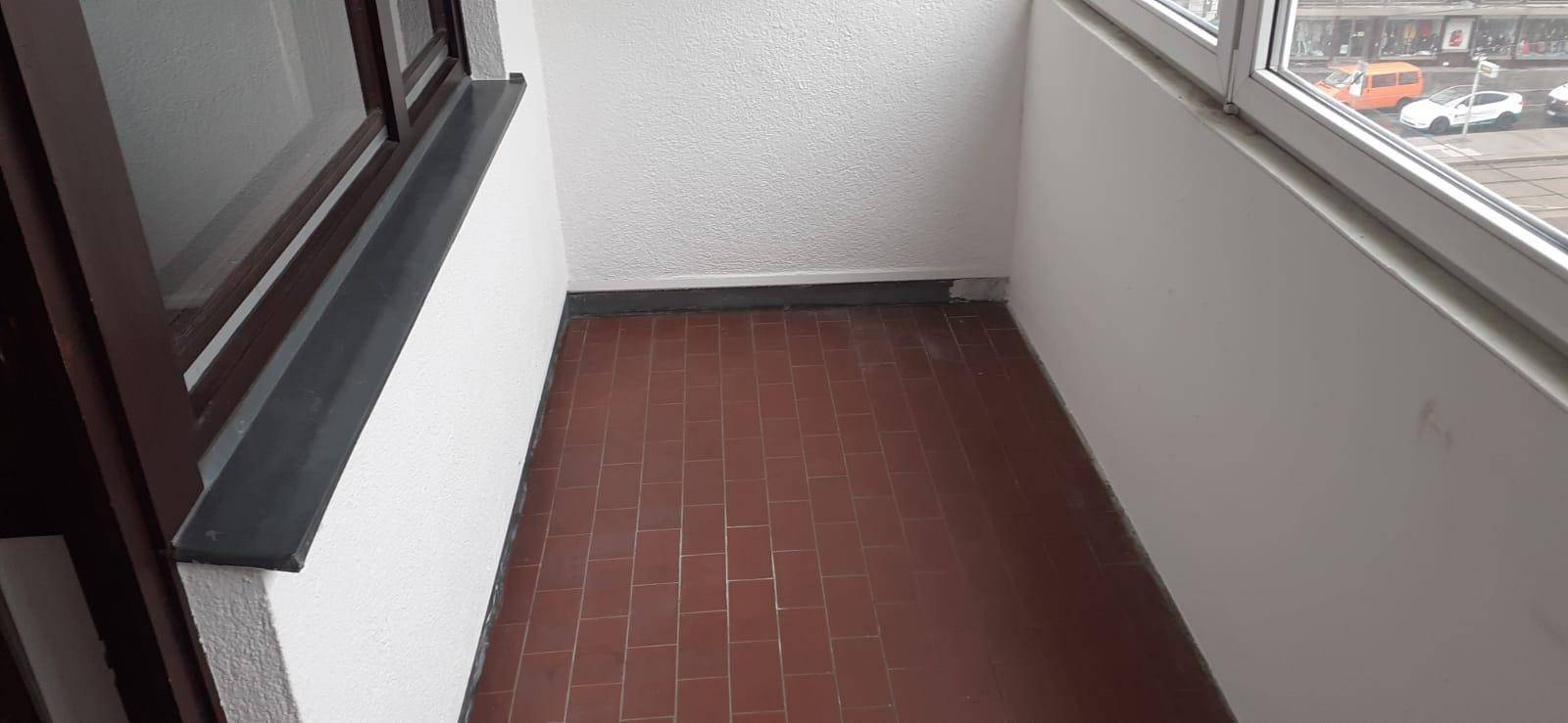 Verglaster Balkon mit braunen Fliesen und Blick auf die Straße und parkende Autos.