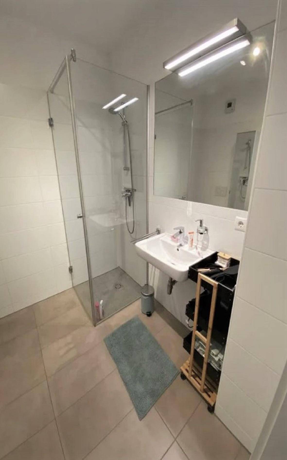 Modernes Badezimmer mit begehbarer Glasdusche, Waschbecken und großem Spiegel.
