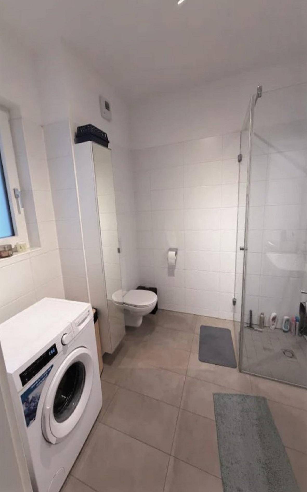 Helles Badezimmer mit Dusche, WC, Waschmaschine und Fenster für natürliche Belüftung.