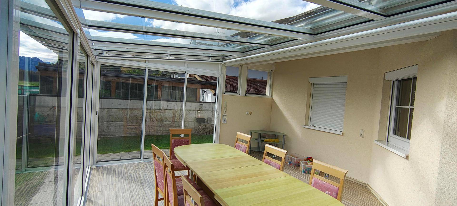 Heller Wintergarten mit Glasdach und Esstisch, ideal für entspannte Stunden.