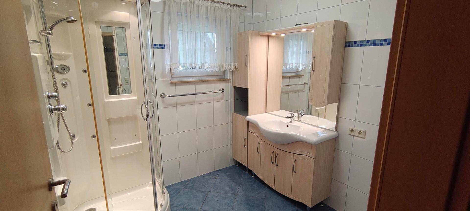 Badezimmer mit Duschkabine, Waschbecken und hellen Fliesen an Wänden und Boden.