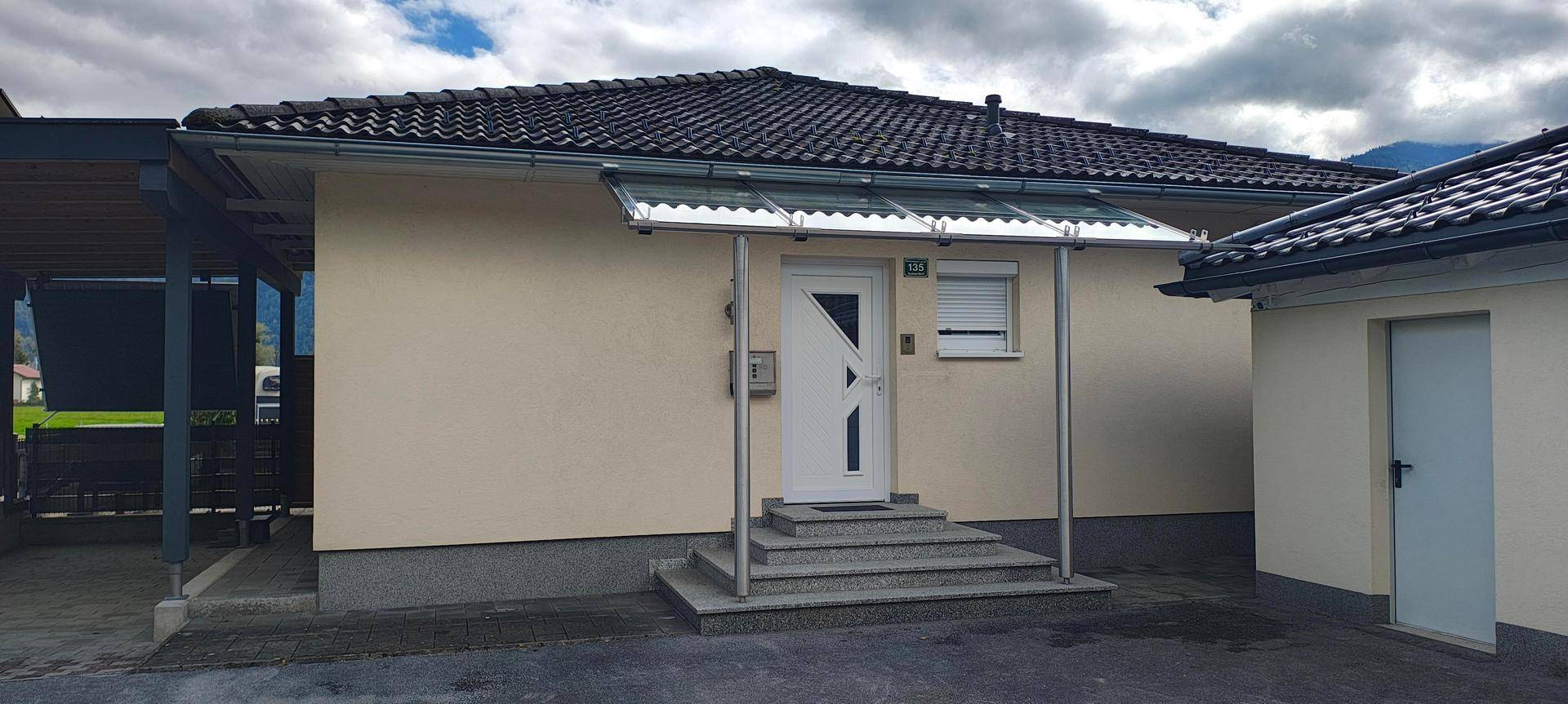 Eingangsbereich des Hauses mit Treppe, Vordach und angrenzendem Carport.