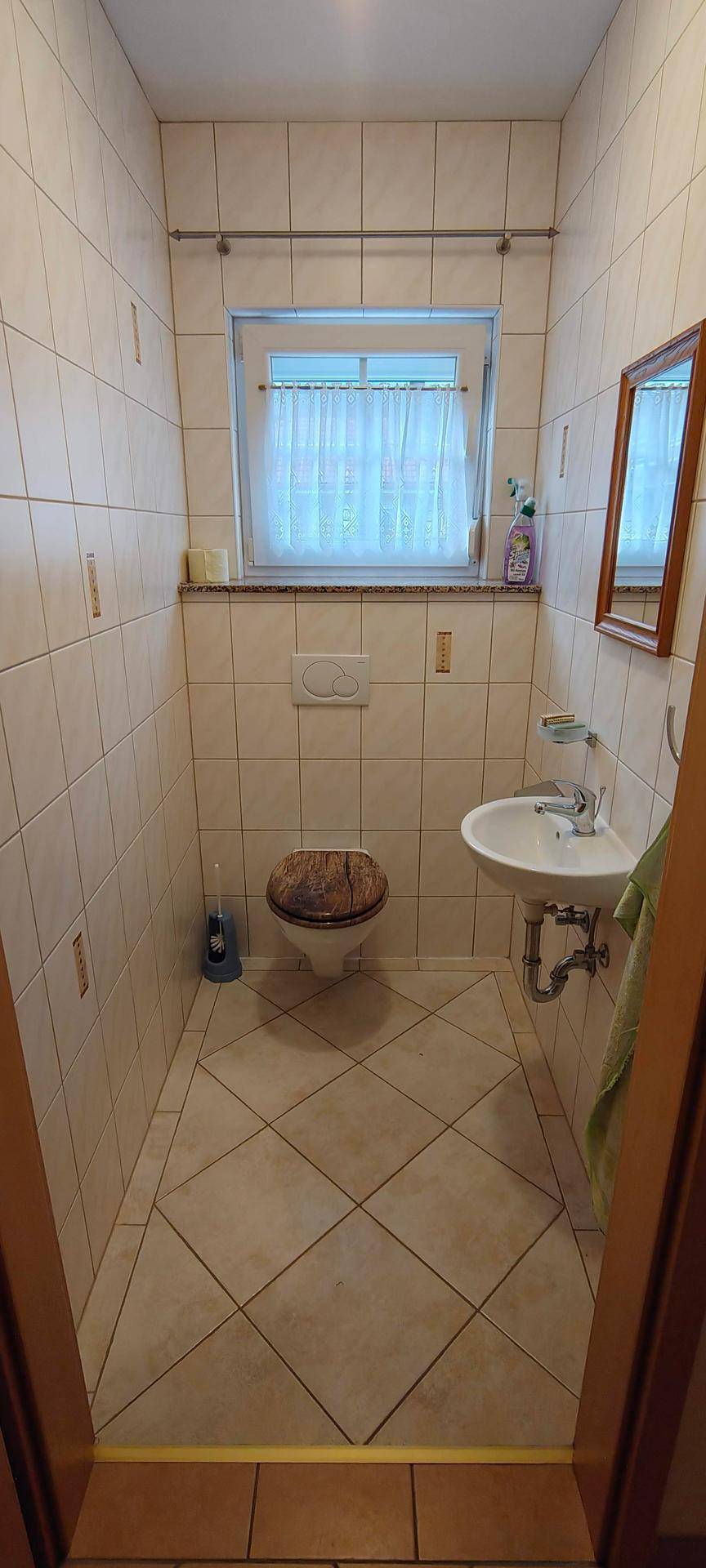 Kleines Gäste-WC mit Fliesen, wandhängendem WC, Waschbecken und Fenster für Belüftung.