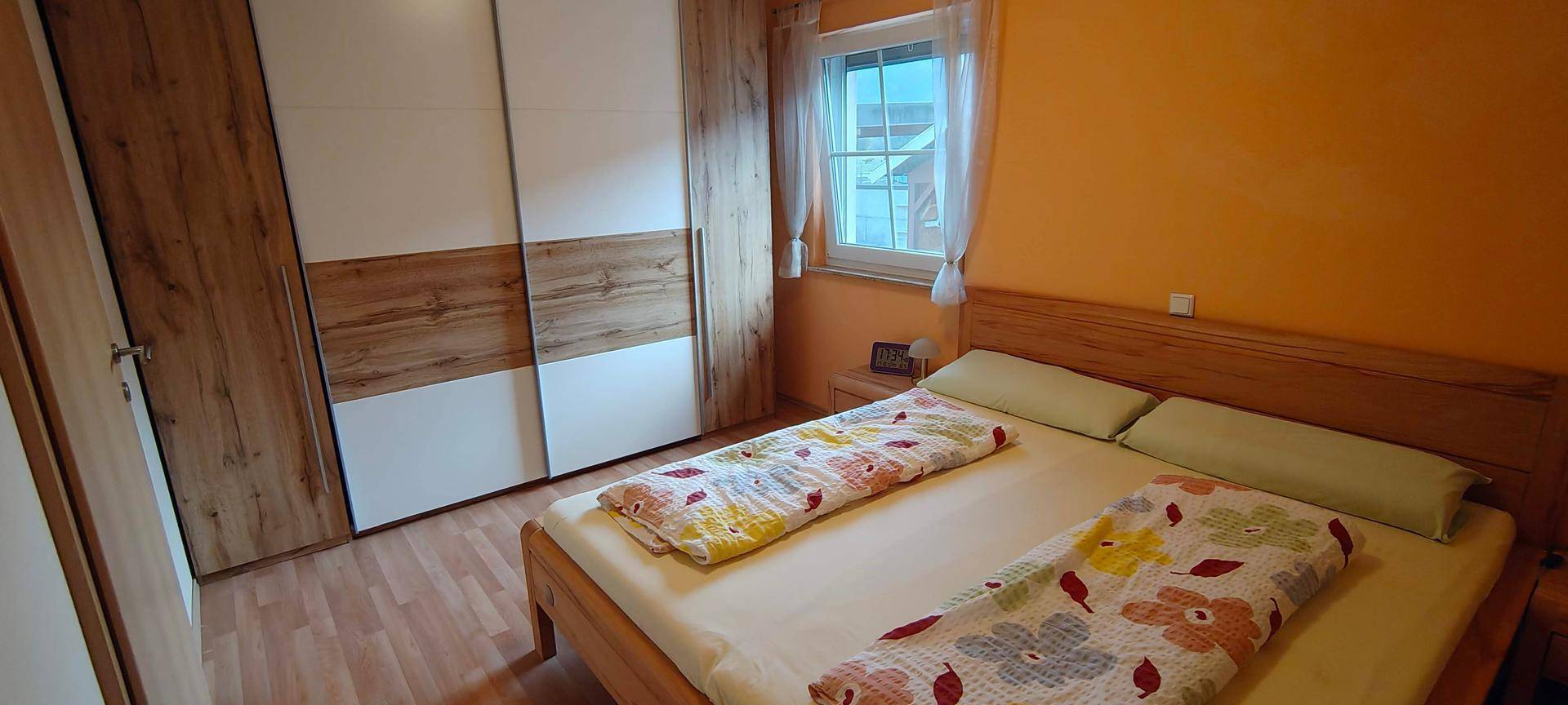 Helles Schlafzimmer mit Laminatboden, großem Kleiderschrank und Fenster für natürliche Belichtung.
