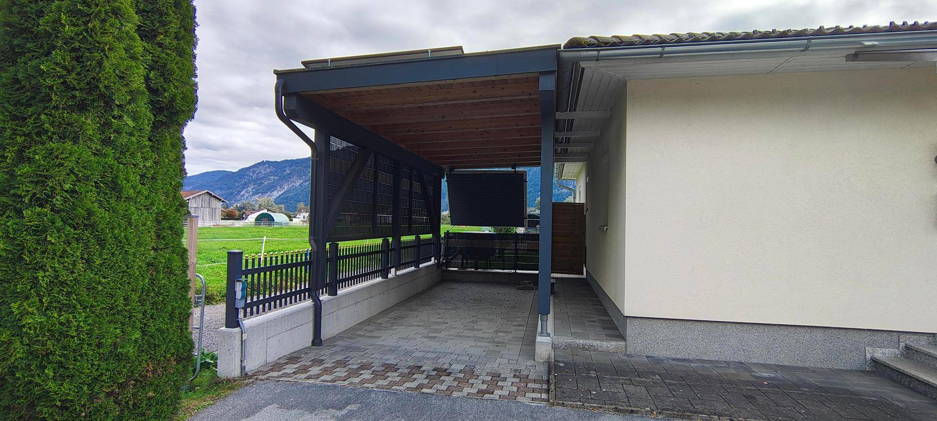 Geräumiger Carport mit Holzdach und Blick auf die umliegende Landschaft und Berge.